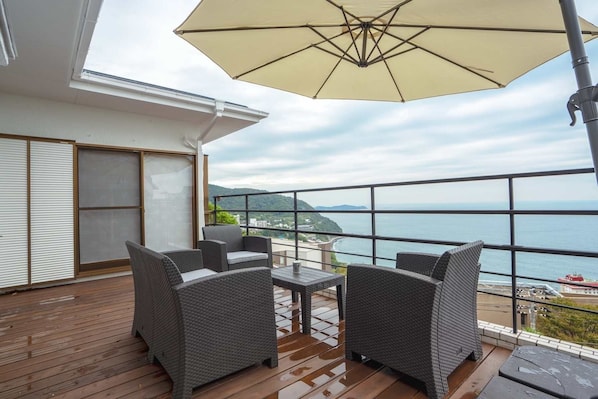 A balcony with wicker furniture and a large umbrella, overlooking a coastal view.
