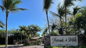 A sign reading "Hacienda de Milpa" with a cobblestone path leading to a building, surrounded by palm trees and greenery. - Hacienda de Mita Golf View Beach Clubs & Golf Cart (Punta de Mita)