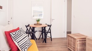 A small, bright room with a wooden floor, a yellow sofa, a small table with chairs, and a wooden crate. - Conqvistador 101 Homes (Lisboa)