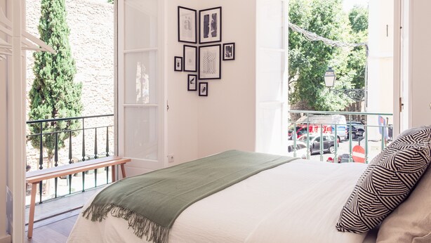 A bedroom with a bed, a green throw blanket, and a view of the street through an open door. - Conqvistador 101 Homes (Lisboa)