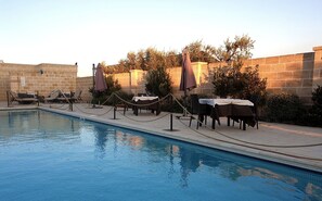 A pool area with lounge chairs and umbrellas, surrounded by stone walls and greenery. - Masseria Sacramento (Palagianello)