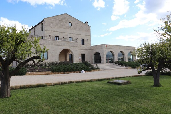 A building with a symmetrical facade, arched windows, and a central entrance with steps leading up to it. - Masseria Sacramento (Palagianello)