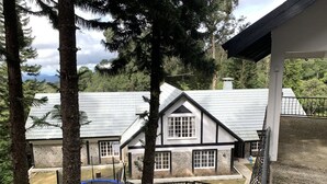 A two-story house with a stone facade and a gabled roof, surrounded by trees and a fenced yard. - Green Acres Fraser's Hill (Raub)