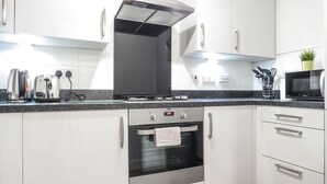 Une cuisine moderne avec des meubles blancs, un four en acier inoxydable, un grille-pain et un four à micro-ondes.