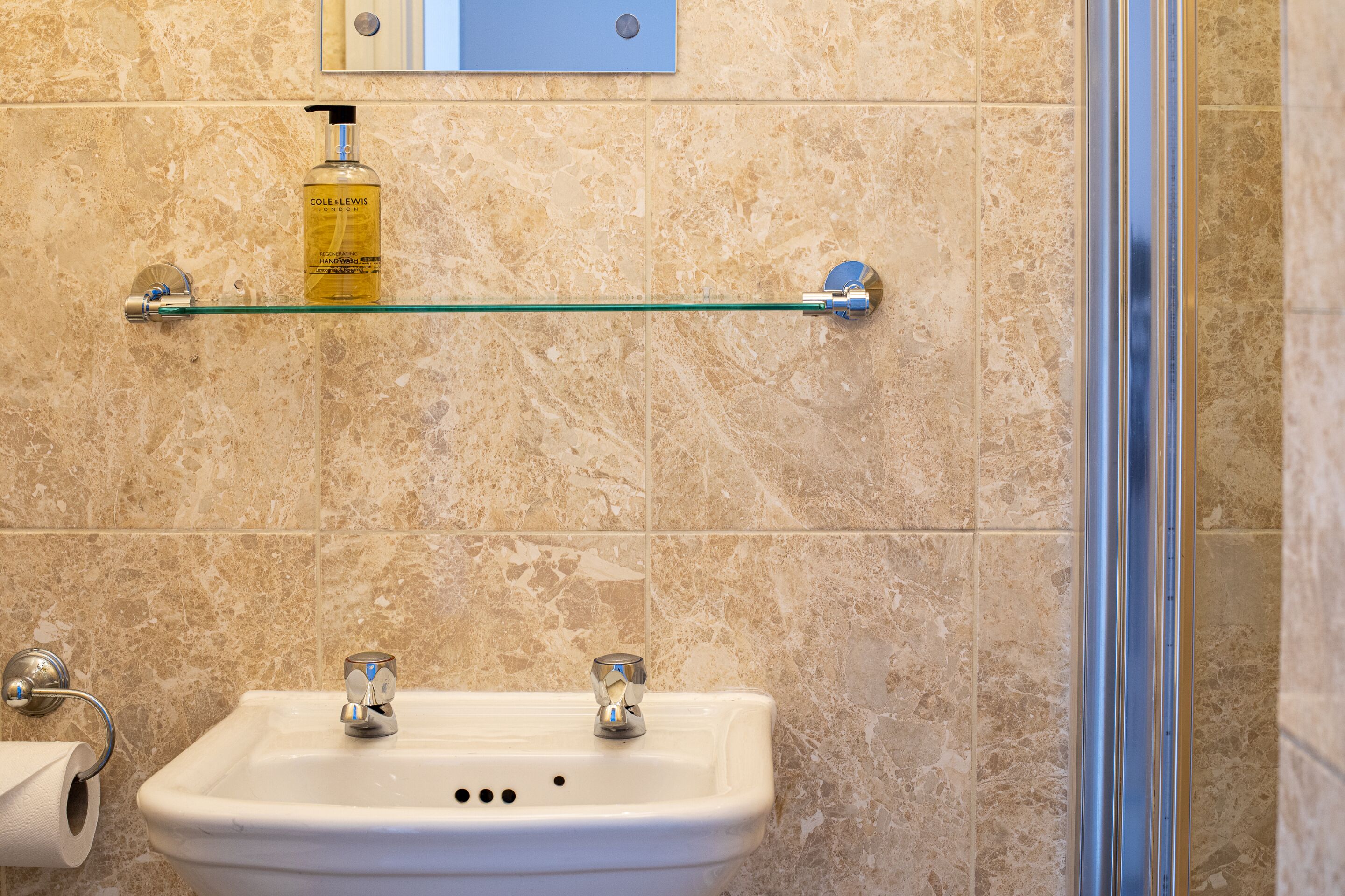 A bathroom with a sink, mirror, and a shelf with toiletries.
