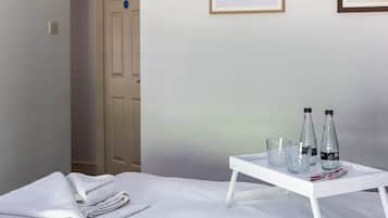 Un letto rifatto con asciugamani piegati, un vassoio con bottiglie e bicchieri, e quadri di pesci appesi al muro.