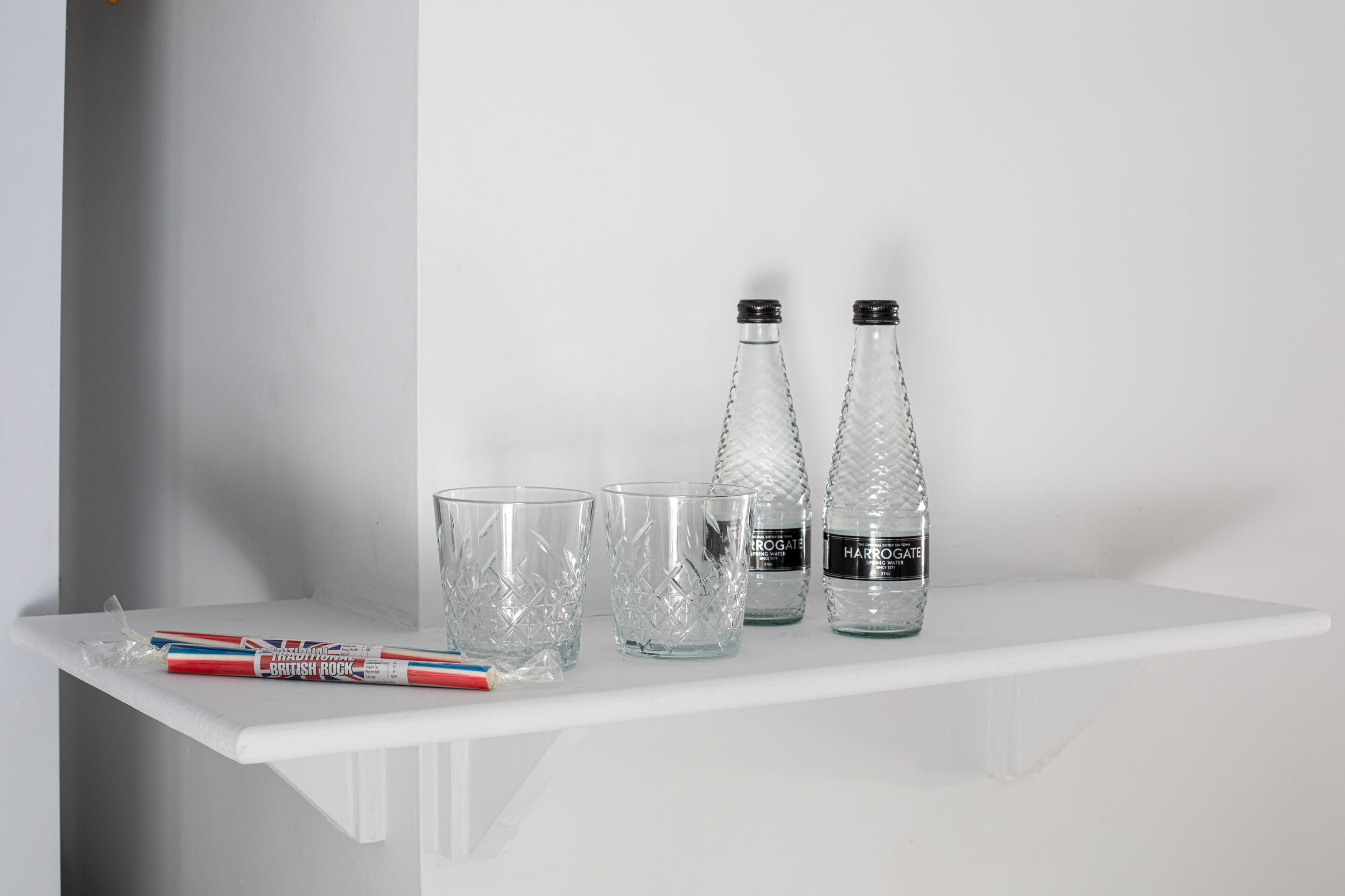Une étagère blanche sur laquelle sont posées deux bouteilles en verre et deux verres transparents.