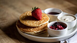 A plate with pancakes, a strawberry, and two small bowls of syrup and berries. - The Spice Ship (Weymouth)