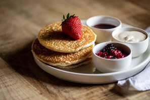 A plate with pancakes, a strawberry, and two small bowls of syrup and berries. - The Spice Ship (Weymouth)