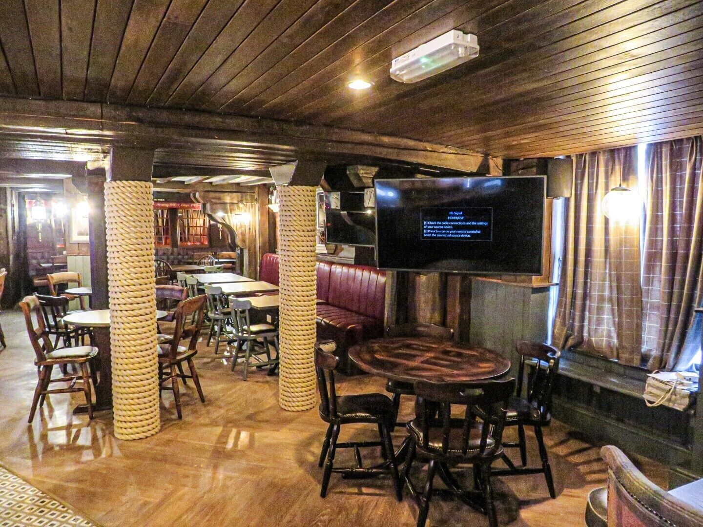 Un restaurant doté d’un plancher en bois, de tables rondes et de banquettes rembourrées. Un téléviseur à écran plat est fixé au mur.