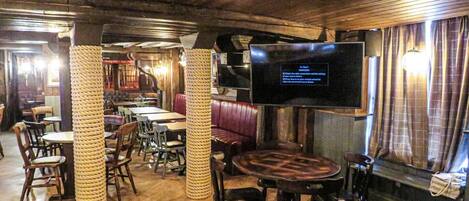 Un restaurant doté d’un plancher en bois, de tables rondes et de banquettes rembourrées. Un téléviseur à écran plat est fixé au mur.