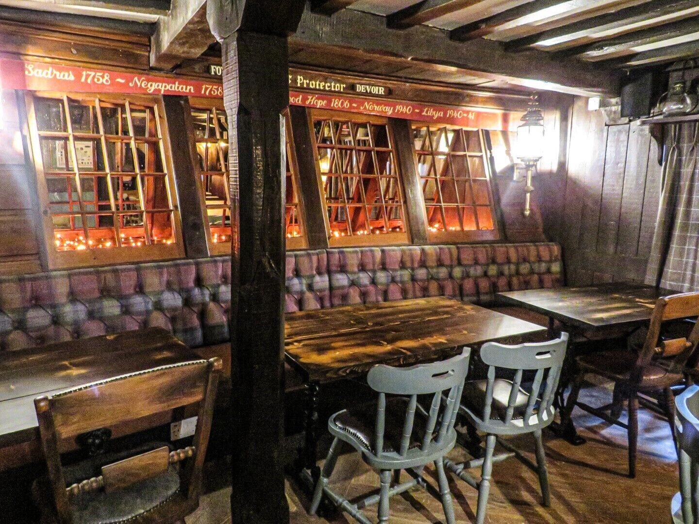Interior acogedor de un restaurante con mesas y sillas de madera, un banco acolchado y una pared que exhibe fechas históricas.