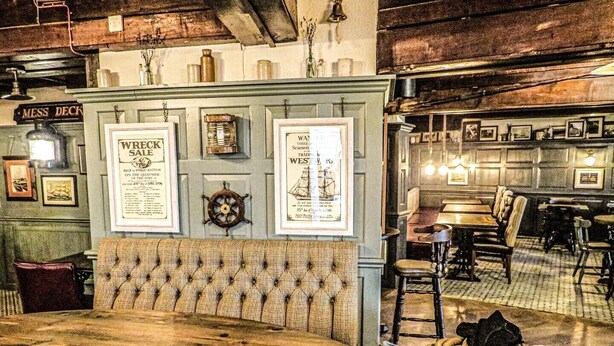 A vintage-themed restaurant interior with a wooden table, cushioned bench, and rope-wrapped stool. - The Spice Ship (Weymouth)