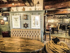 A vintage-themed restaurant interior with a wooden table, cushioned bench, and rope-wrapped stool. - The Spice Ship (Weymouth)