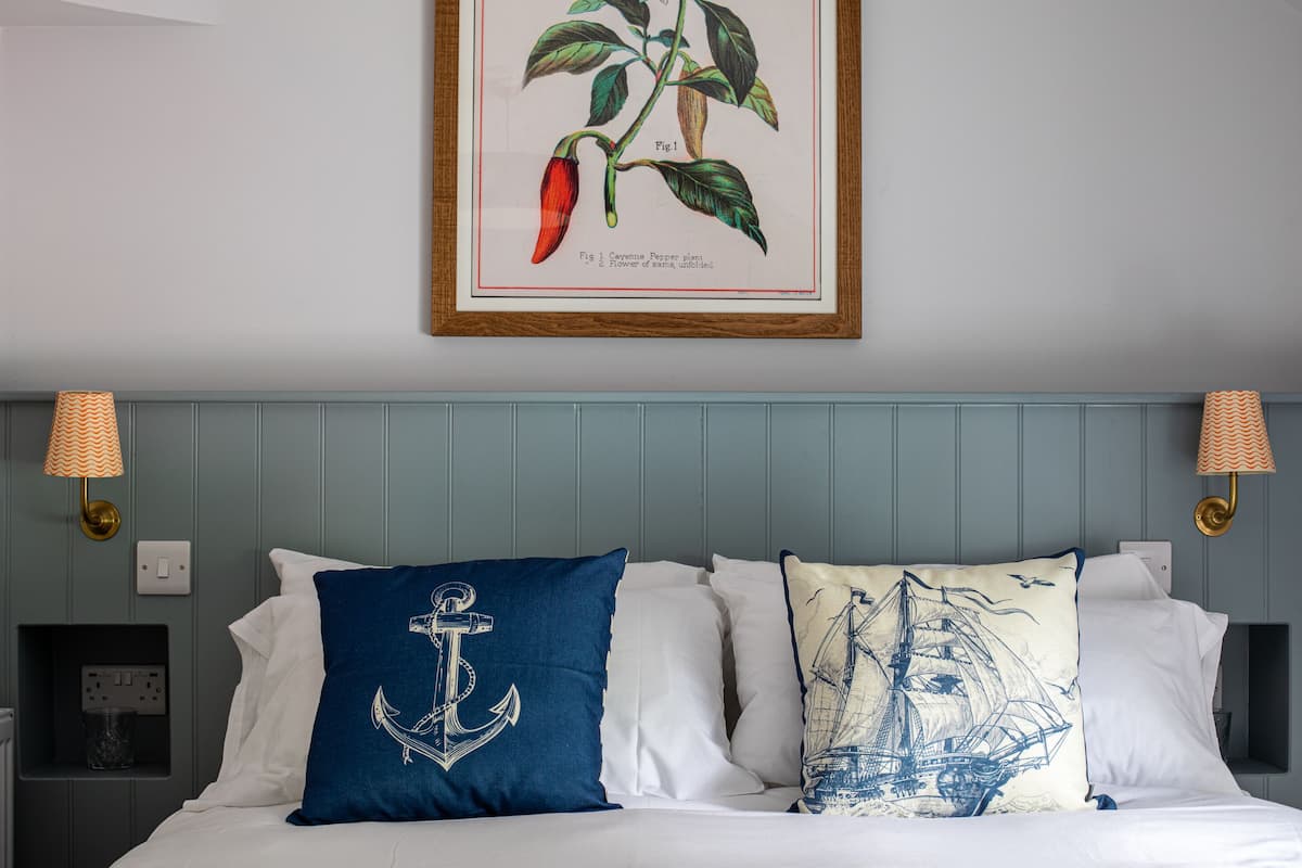 A neatly made bed with white linens and decorative pillows, including one with an anchor design.