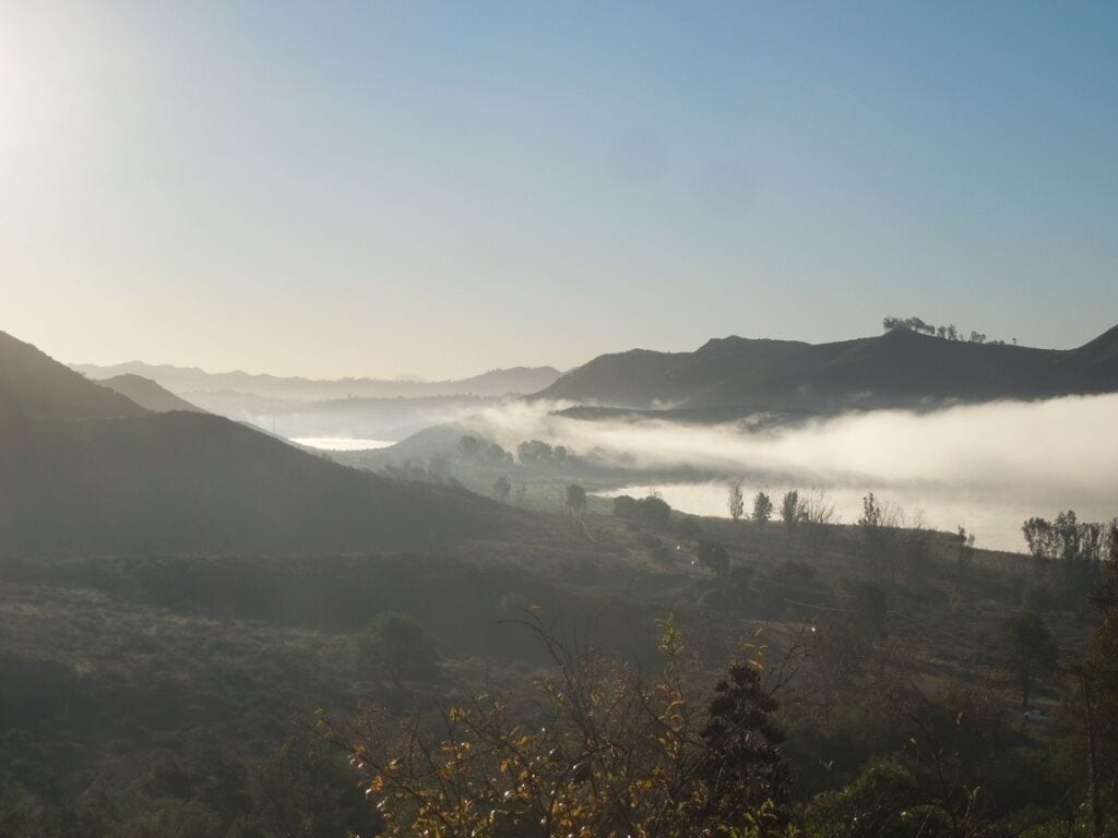A mountainous landscape with a valley and a body of water partially obscured by mist.