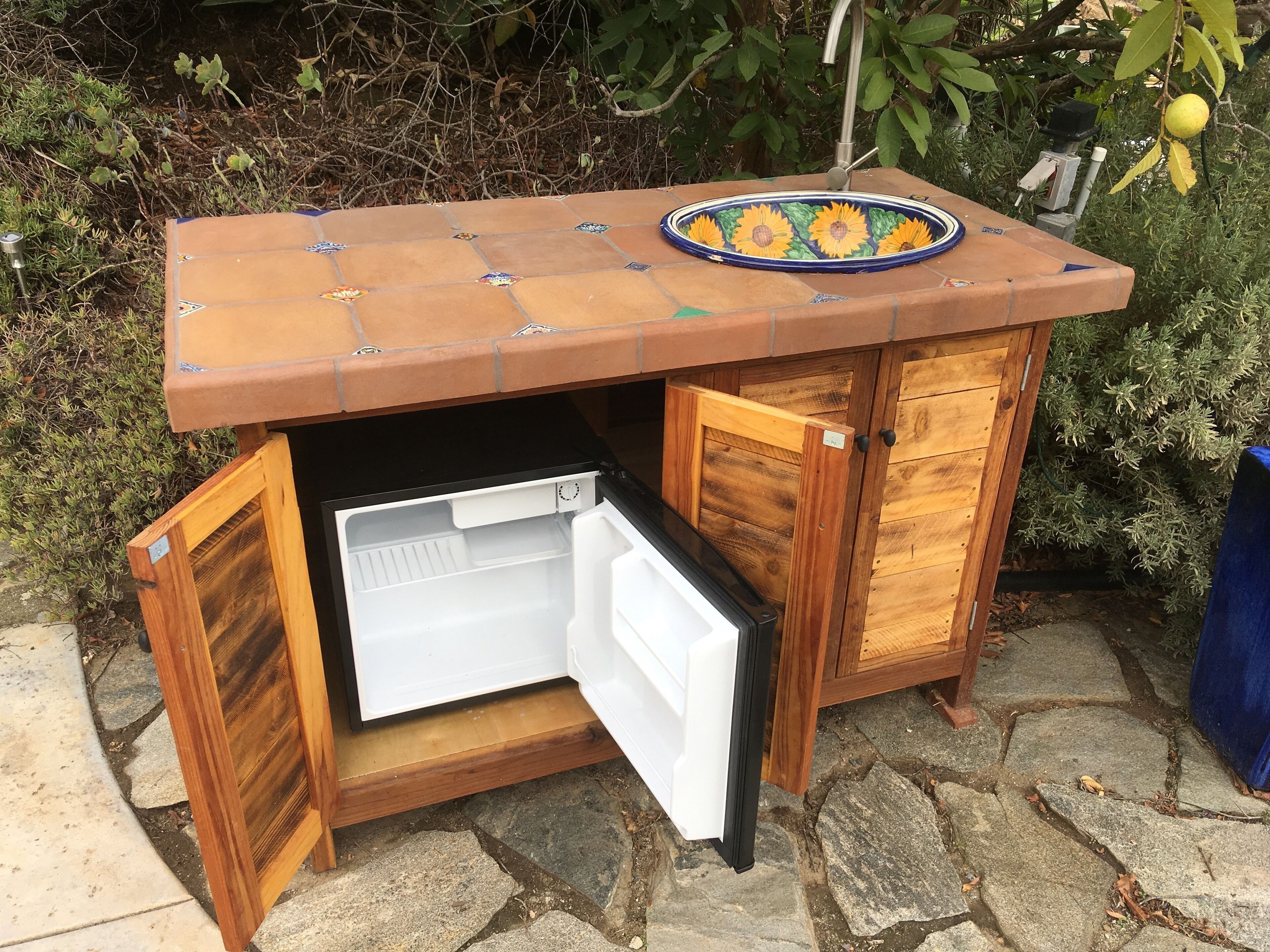 Une structure compacte en bois, dotée d’un réfrigérateur intégré, d’un petit évier et d’une assiette décorative sur le dessus.
