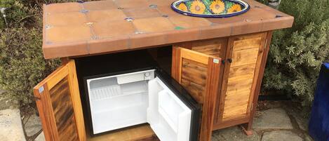 Une structure compacte en bois, dotée d’un réfrigérateur intégré, d’un petit évier et d’une assiette décorative sur le dessus.