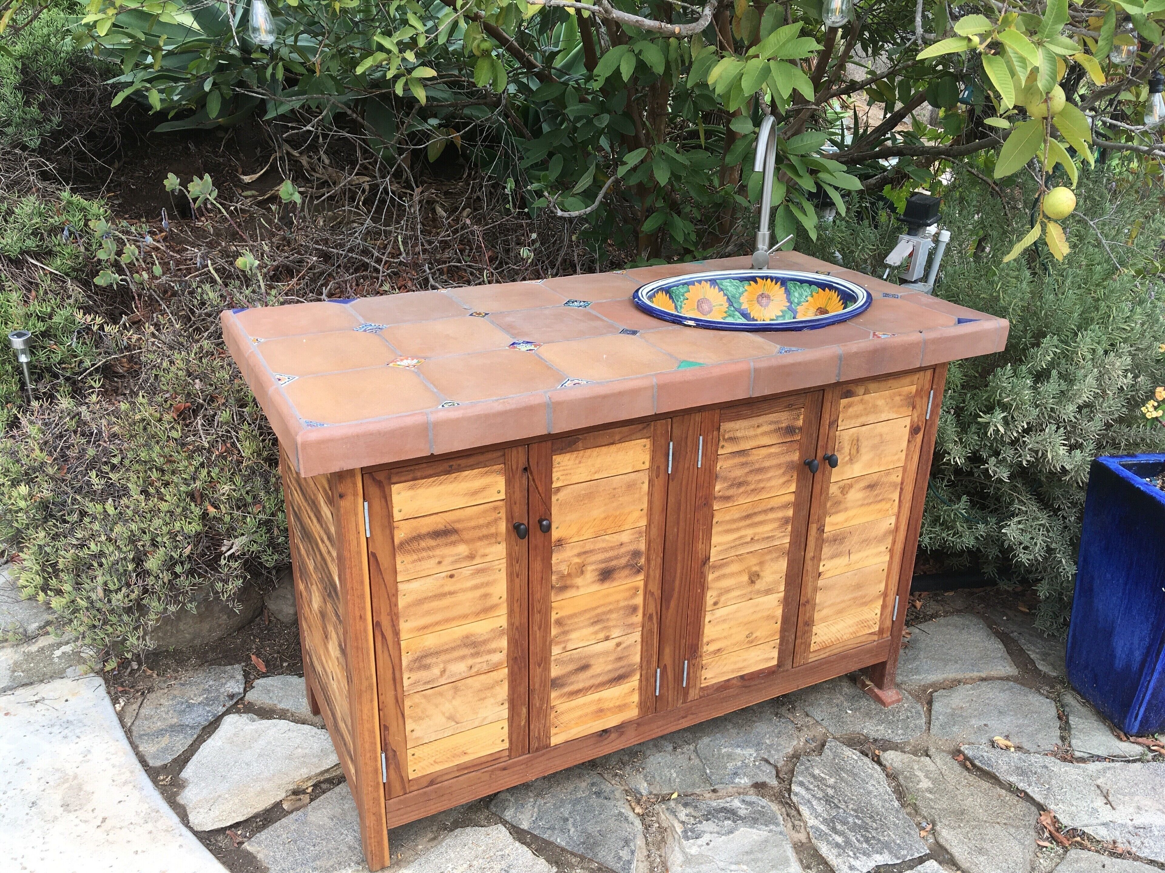 A wooden outdoor bar with a tiled countertop and a sink.