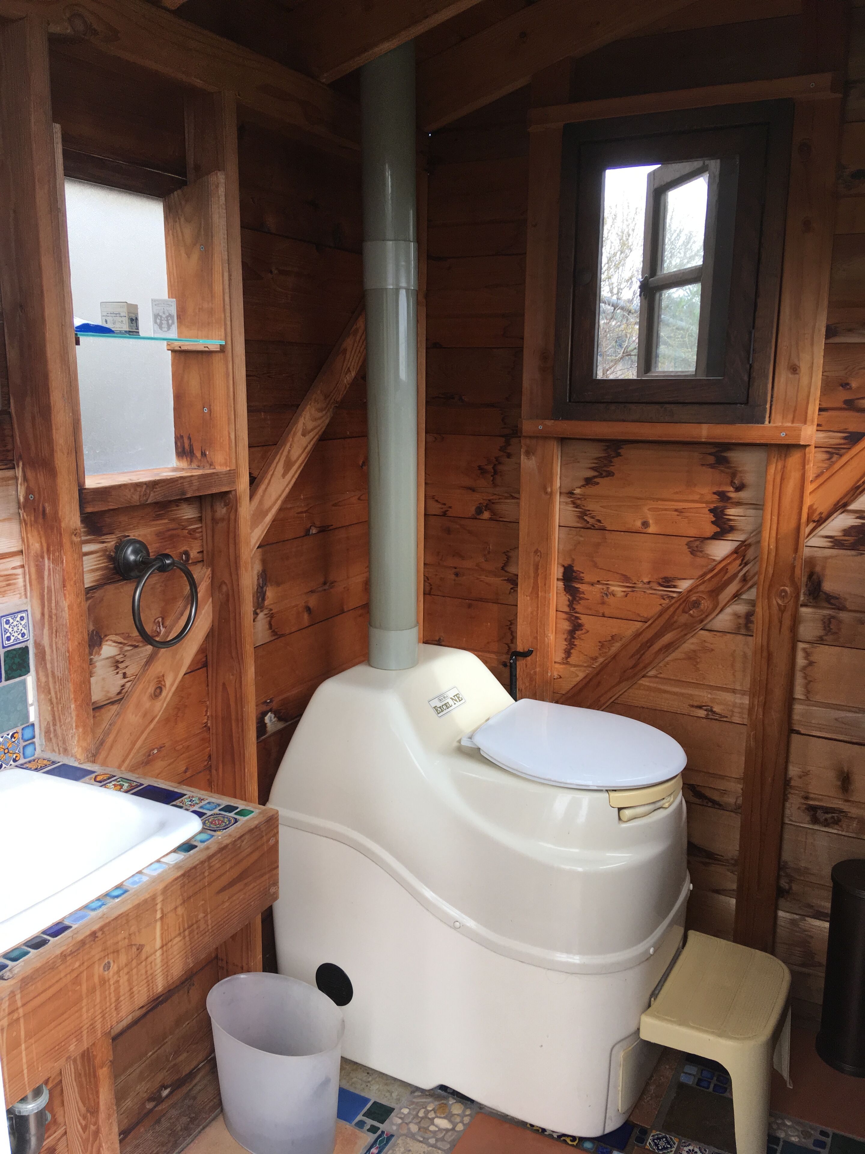A wooden cabin bathroom with a toilet, sink, and window.