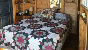 Ein Schlafzimmer einer Holzhütte mit einem Bett, einer Steppdecke, Regalen mit Flaschen, einer Karte und einer Tür.