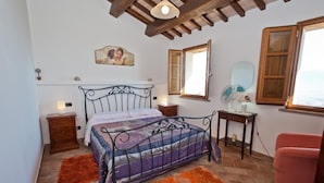 A bedroom with a bed, two nightstands, a wooden cabinet, a window, and a mirror. - B&B Madonna Del Latte (Cannara)