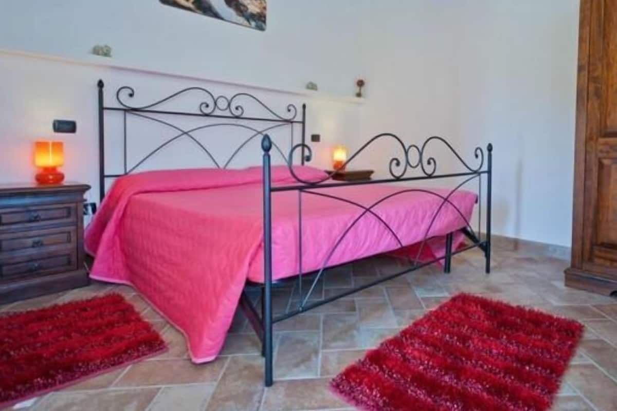 A bedroom with a metal bed frame, pink bedding, two bedside lamps, a red rug, and a wooden cabinet.