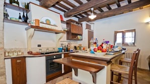A kitchen with a central island, wooden chairs, a built-in oven, and various kitchen items on shelves. - B&B Madonna Del Latte (Cannara)