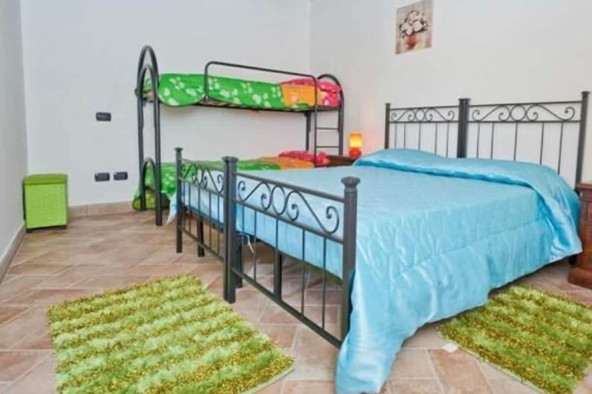 A room with bunk beds, a green trash bin, and a blue bedspread.