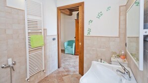 A bathroom with a white bathtub, a towel rack with a green towel, a wooden door, and a tiled floor. - B&B Madonna Del Latte (Cannara)