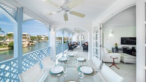 Un comedor con vista al agua, muebles blancos y un ventilador de techo.