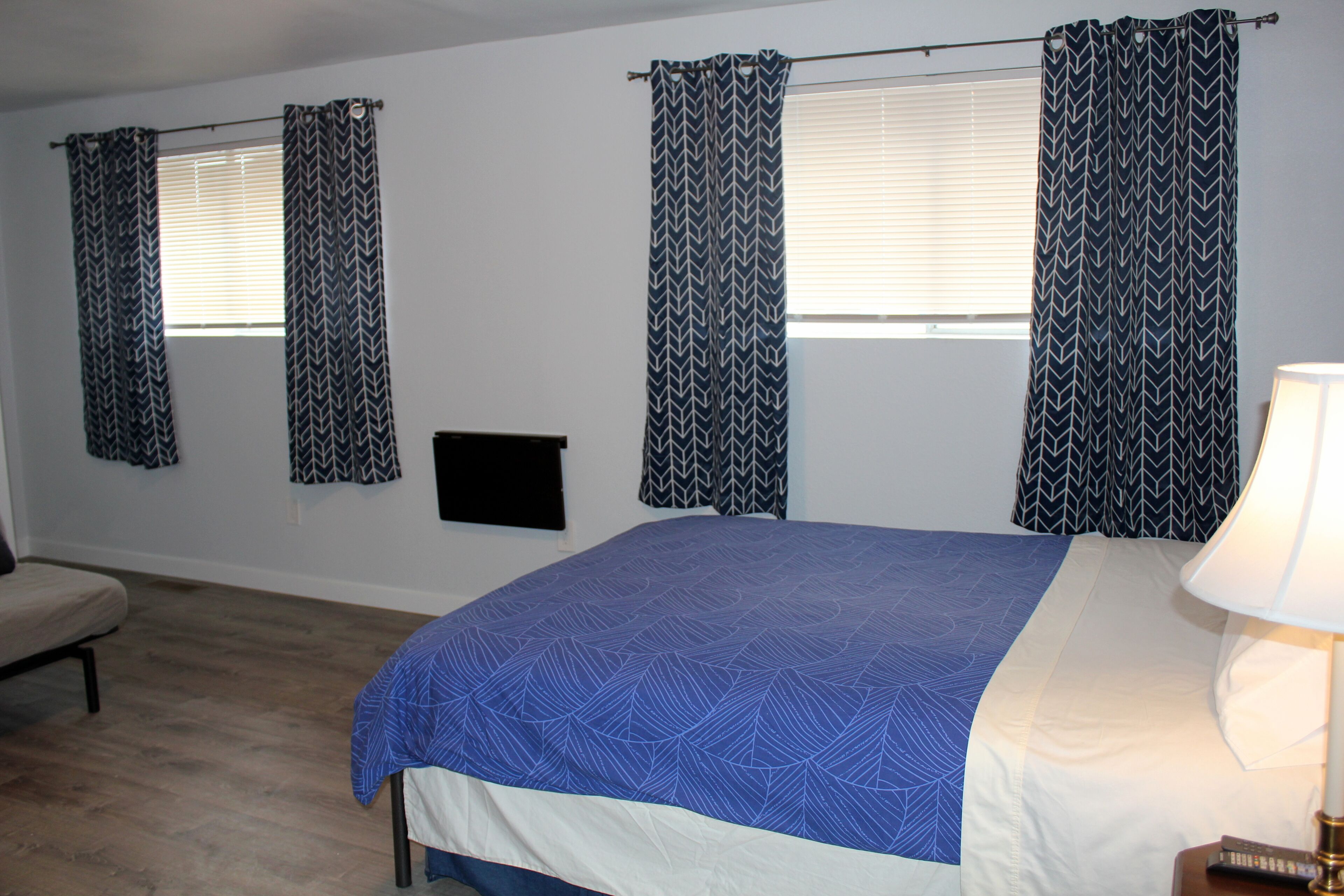 A bedroom with a bed, a bedside table with a lamp, a chair, and a window with curtains.
