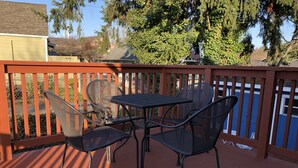 A patio with a table and chairs, a red railing, and a view of trees and a house in the background. - Rainier Guesthouse (Walk to Metro) (Seattle)