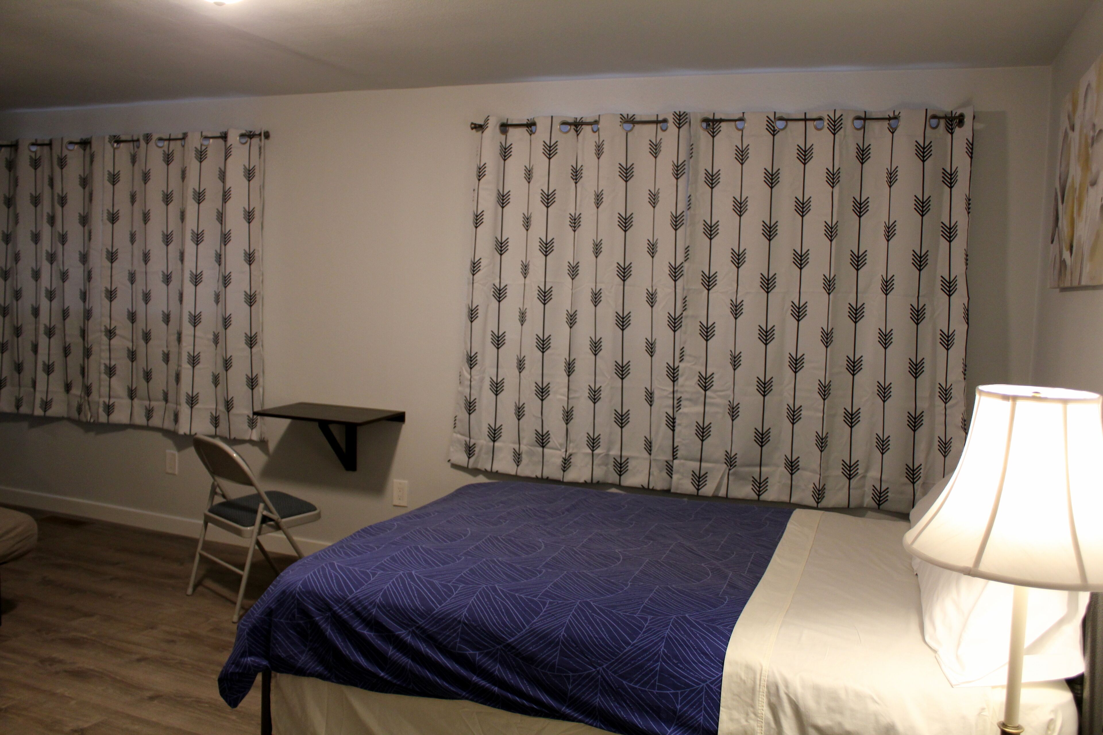 Una habitación con cama, silla, escritorio y cortinas.