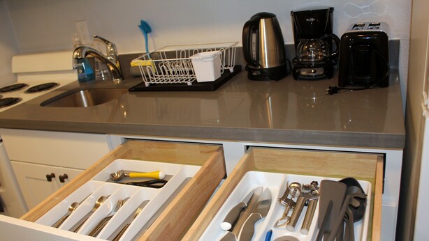A kitchen with a stainless steel sink, a coffee maker, and a toaster. There is a drawer with utensils and a dish rack on the counter. - Rainier Guesthouse (Walk to Metro) (Seattle)