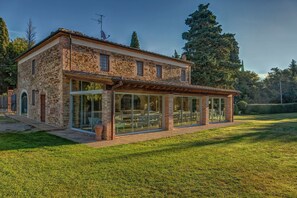 A stone house with large glass windows and a patio area. - Fienile - Apartment with pool (Montaione)