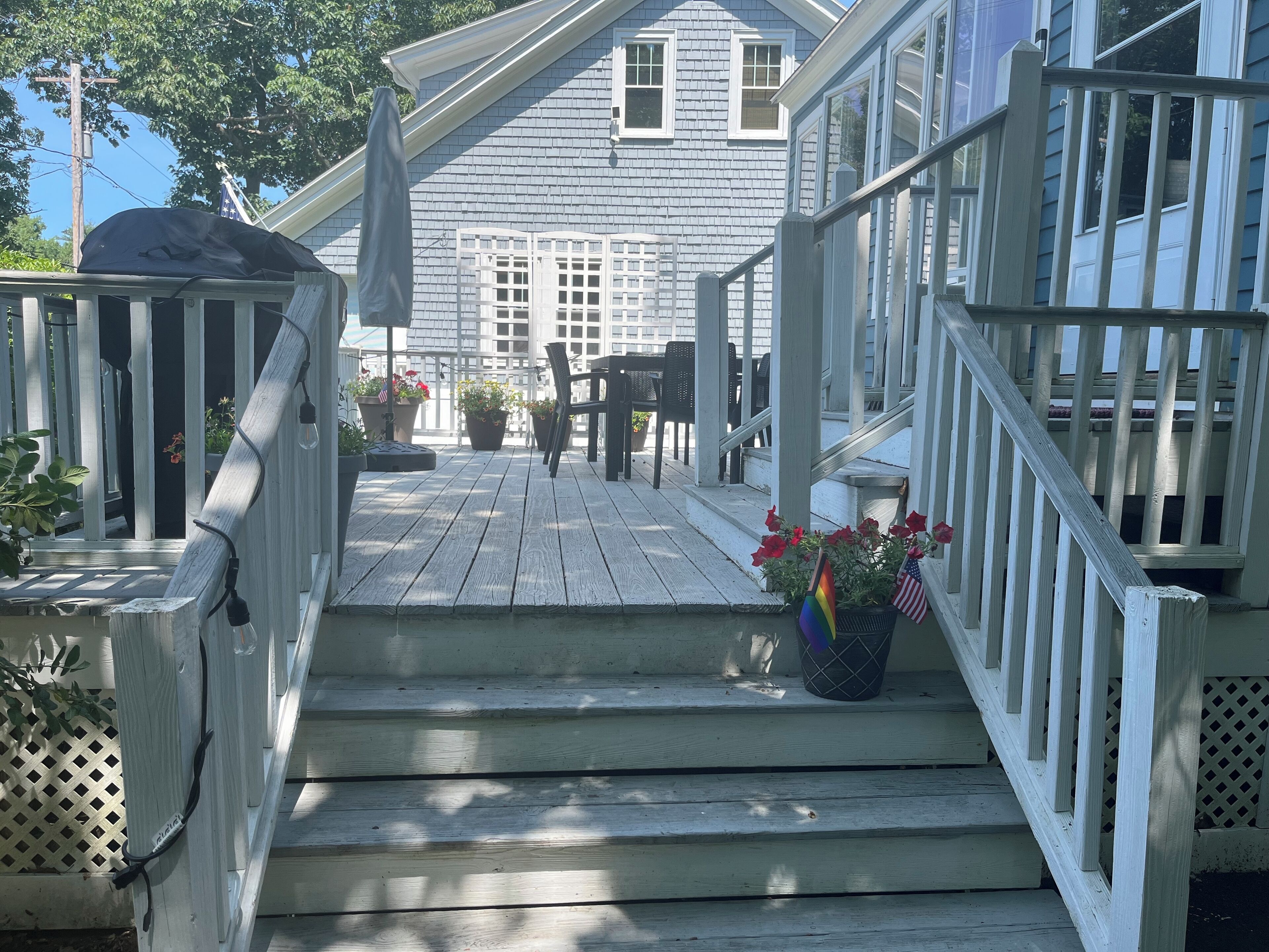 A wooden deck with steps leading to a house. There are potted plants and a flag on the deck.