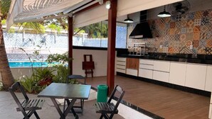 Ein Essbereich im Freien mit Blick auf einen Pool, Holzboden und einer gefliesten Spritzschutzleiste in der angrenzenden Küche.
