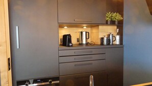 Eine kompakte Küche mit Kaffeemaschine, Wasserkocher und einer kleinen Topfpflanze auf der Arbeitsplatte.