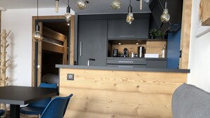 Eine moderne Küche mit Holzschnitzereien, einem eingebauten Backofen und einer Kaffeemaschine. Es gibt einen Essbereich mit einem Tisch und blauen Stühlen.