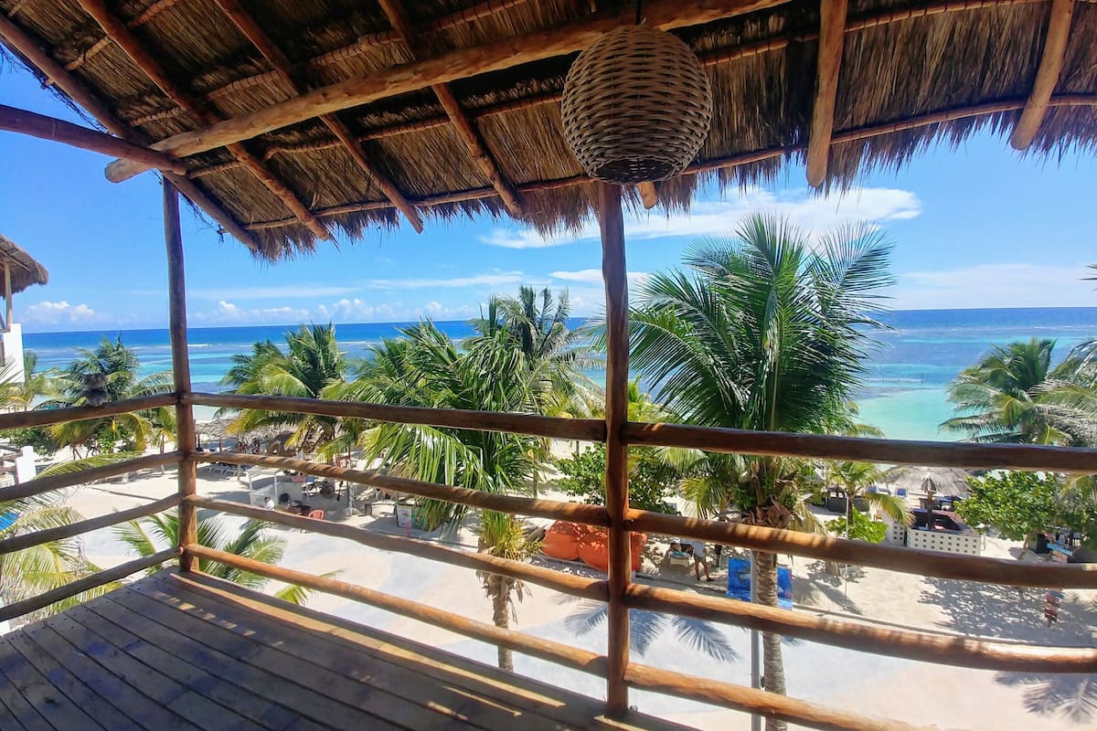 A wooden deck with a thatched roof overlooking a beach.