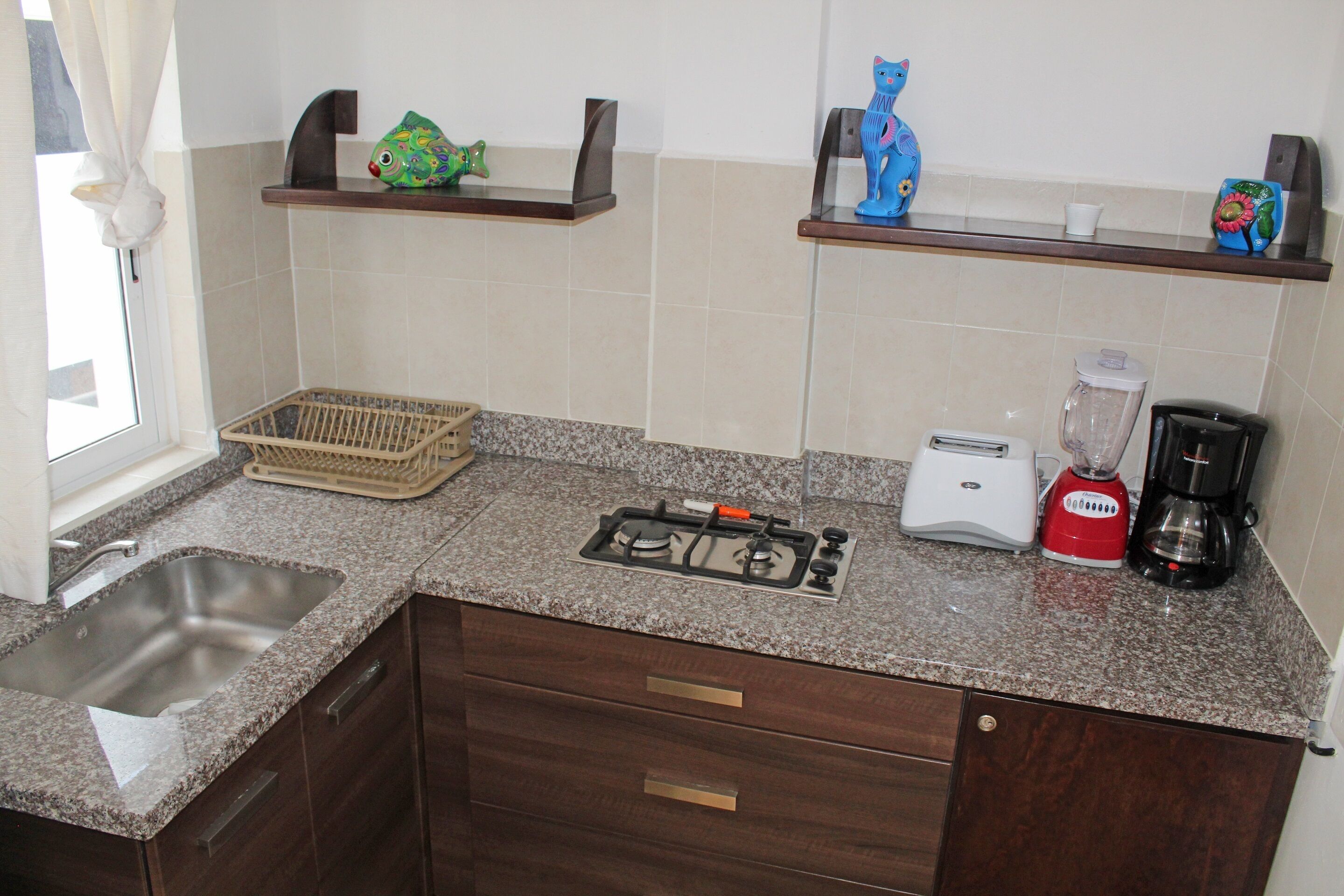 A kitchen with a granite countertop, a gas stove, a toaster, a blender, and shelves with decorative items.