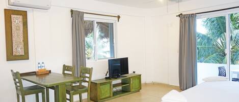 Habitación de hotel con cama, televisor sobre una cómoda de madera, una mesa de comedor con sillas y una ventana con cortinas.