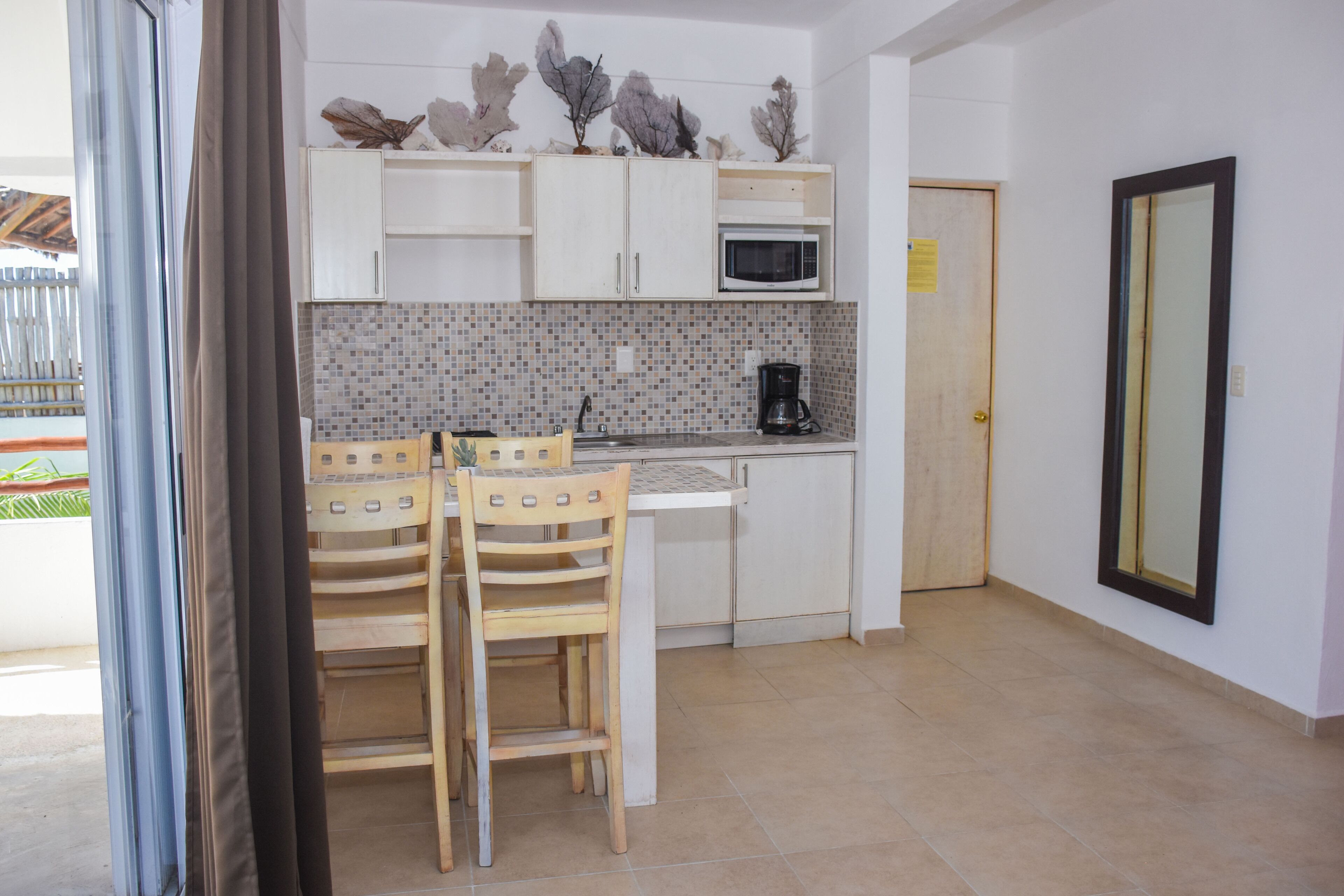 Cocina compacta con armarios blancos, microondas, cafetera y una zona de comedor con dos sillas.