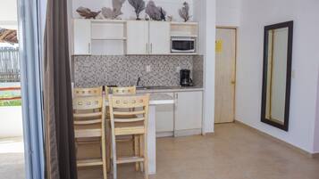 Cocina compacta con armarios blancos, microondas, cafetera y una zona de comedor con dos sillas.