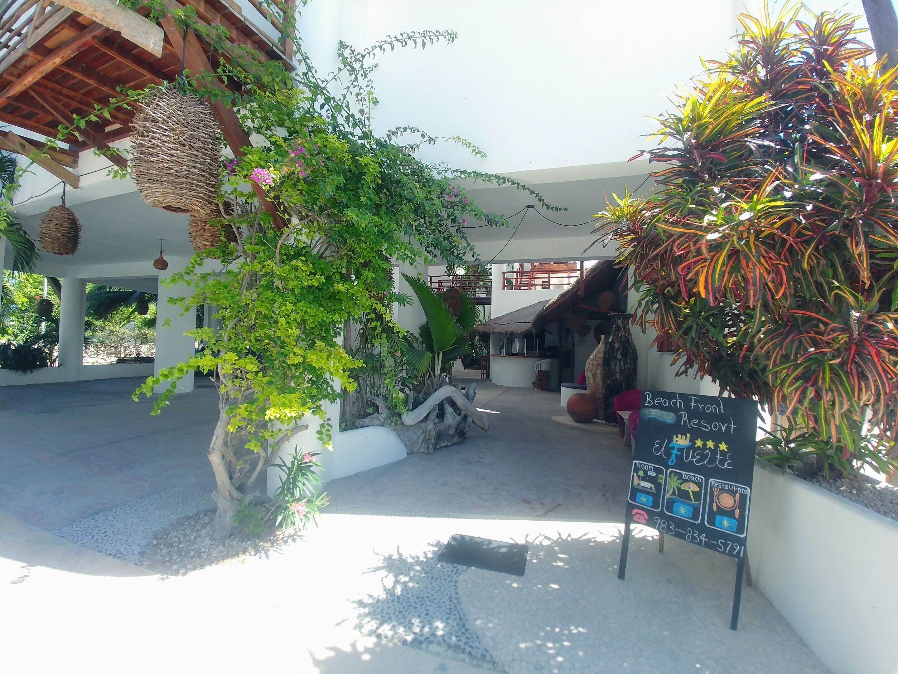 A resort entrance with a signboard indicating amenities like beach, room, and restaurant.