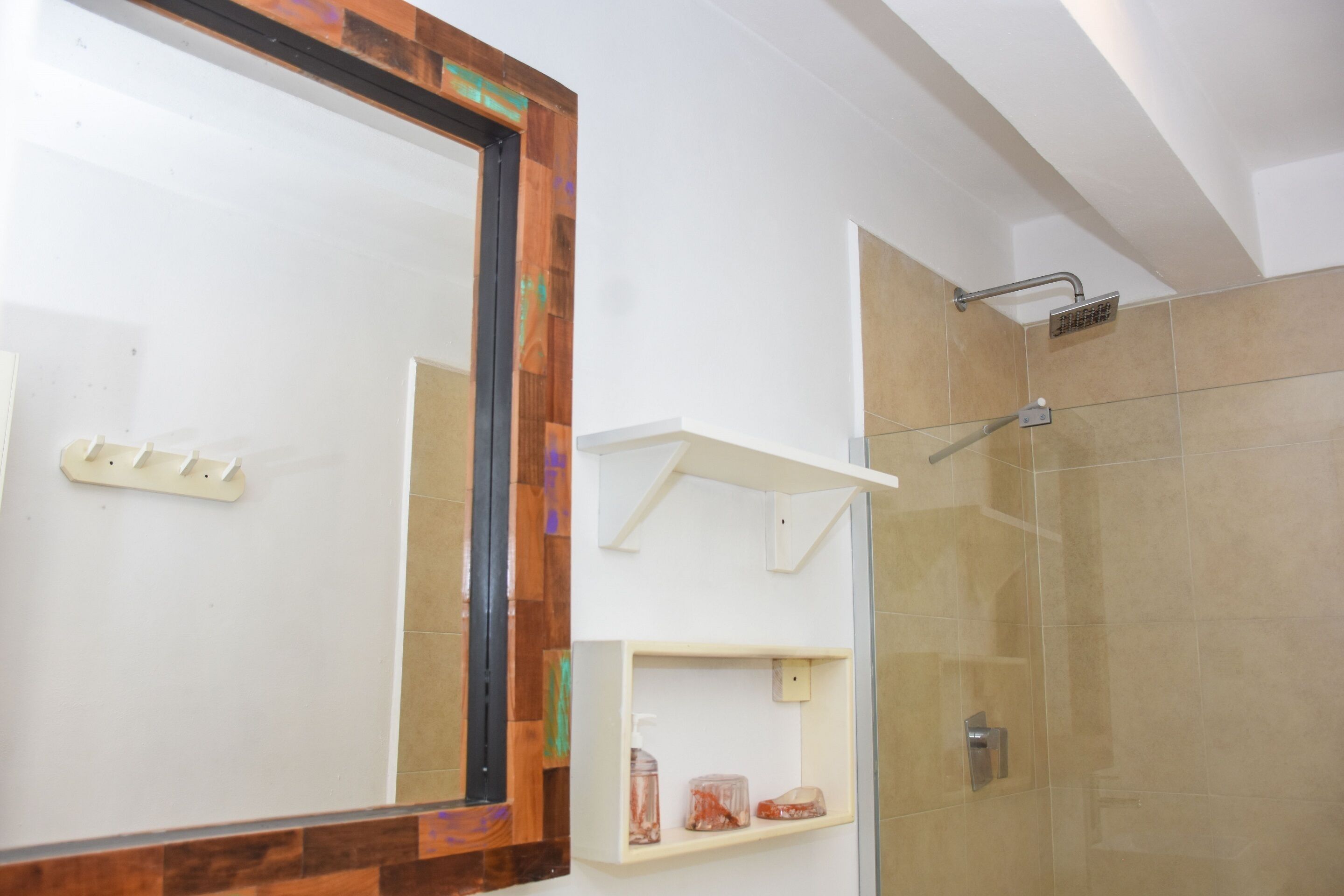 A bathroom with a large mirror, a shower, and a shelf with toiletries.