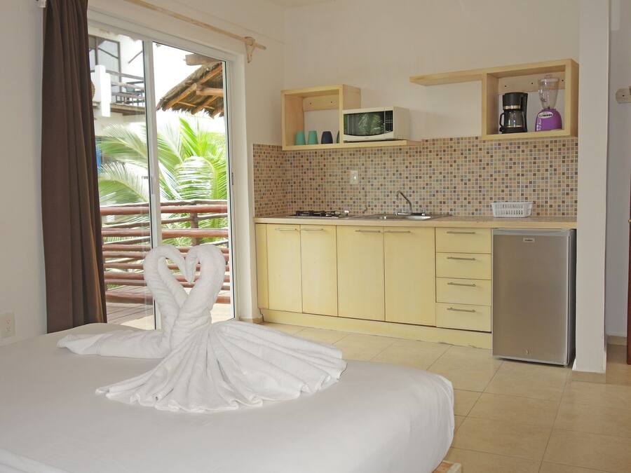 A hotel room with a bed, a kitchenette, a refrigerator, and a view of palm trees.