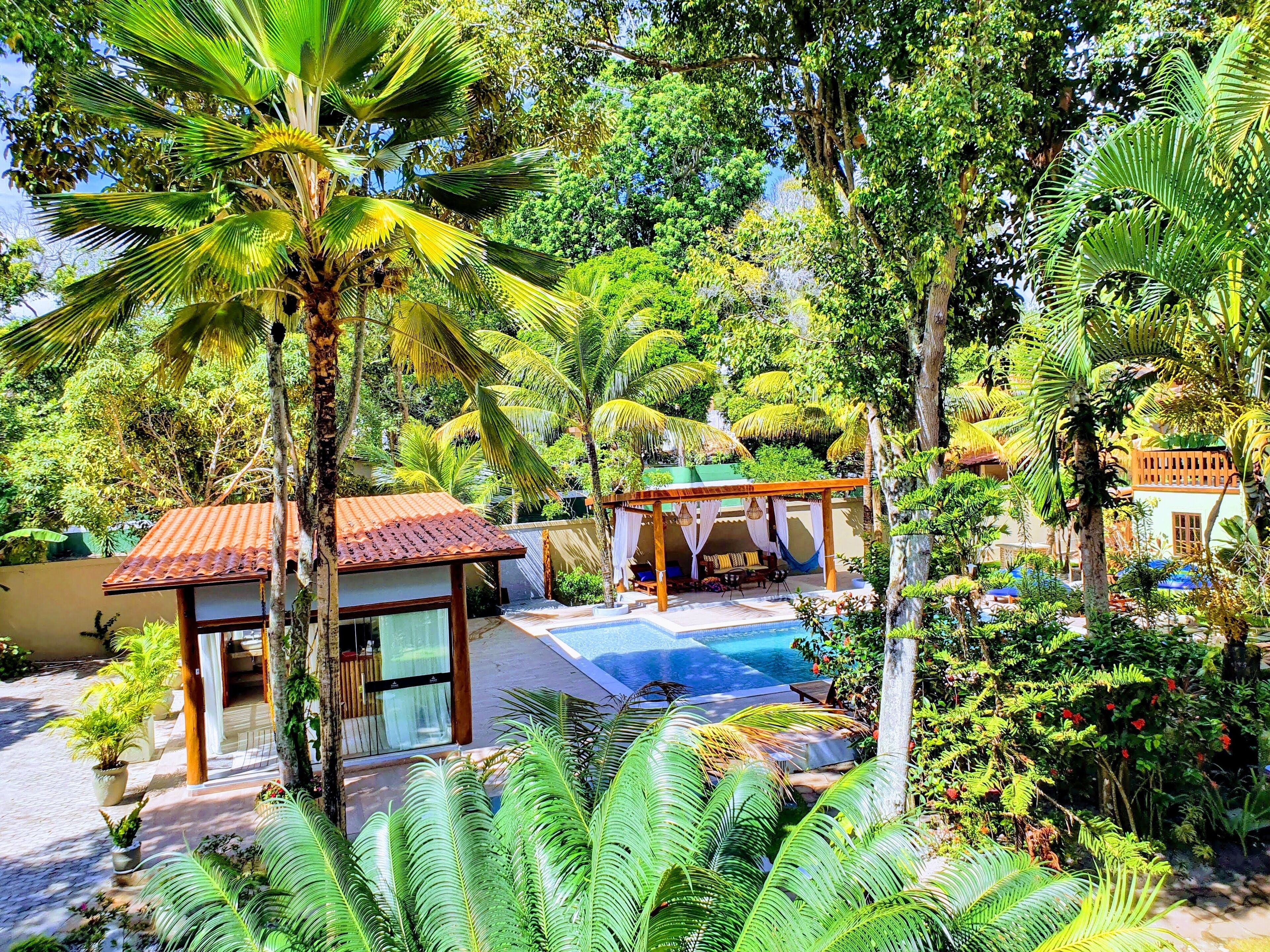 A tropical resort with a swimming pool, palm trees, and a covered seating area.
