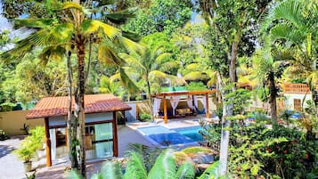 A tropical resort with a swimming pool, palm trees, and a covered seating area.
